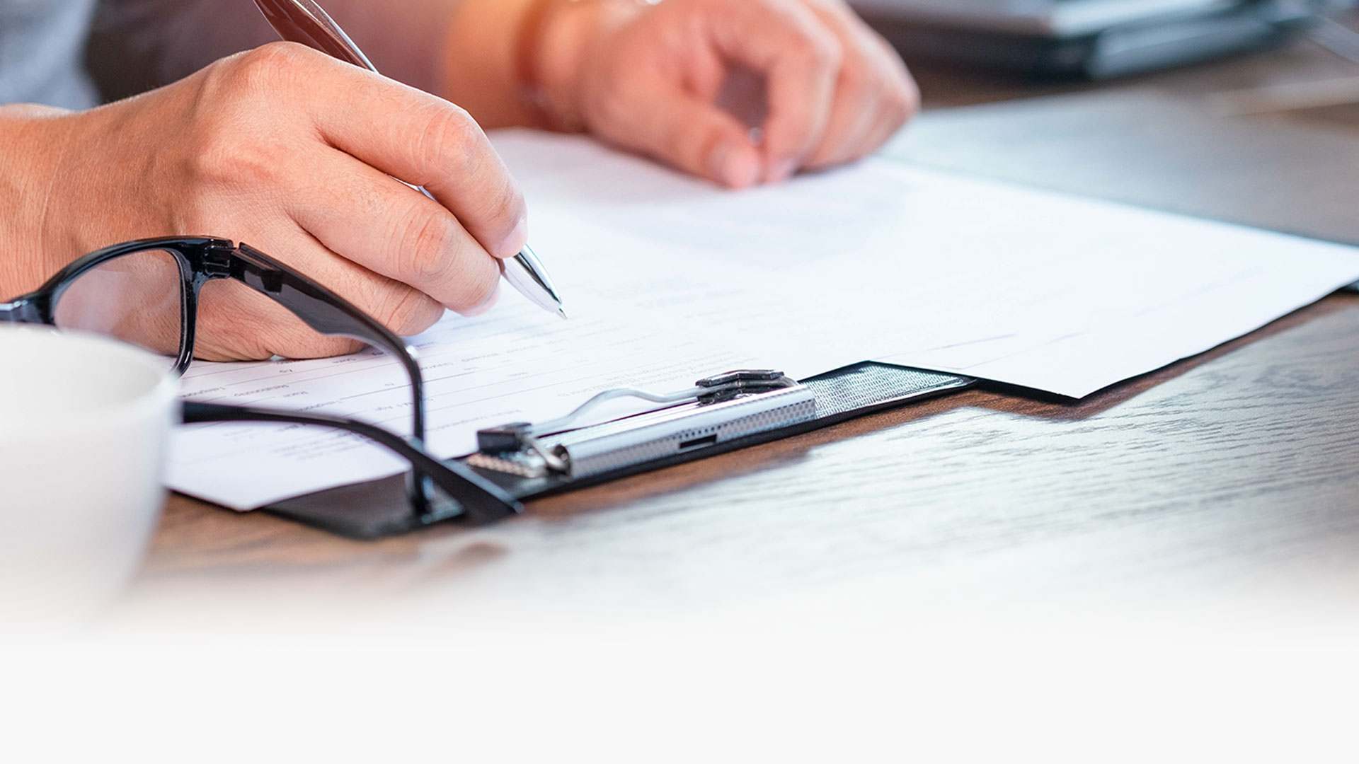 Hand holding a pen writing on a clipboard.